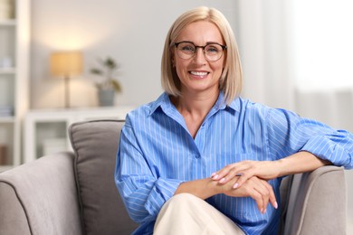 Portrait of smiling middle aged woman sitting on armchair at home