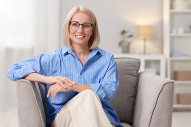 Photo of Portrait of smiling middle aged woman sitting on armchair at home