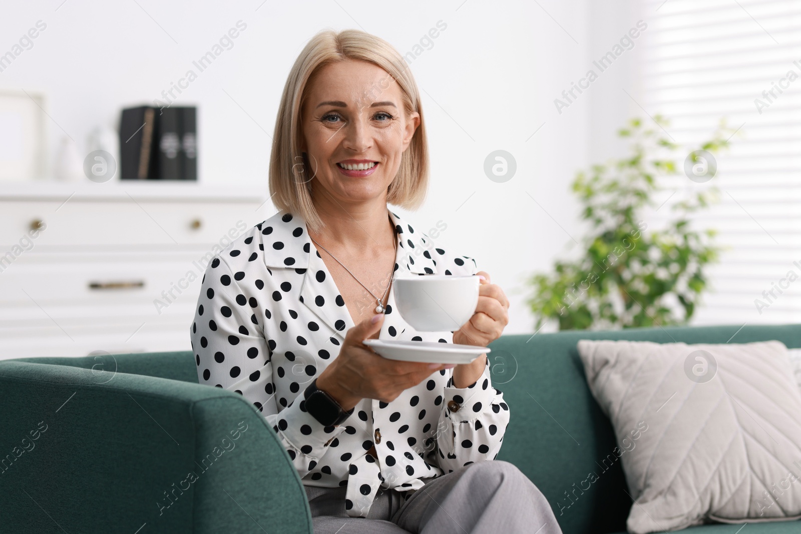 Photo of Smiling middle aged woman with cup of hot drink on sofa at home