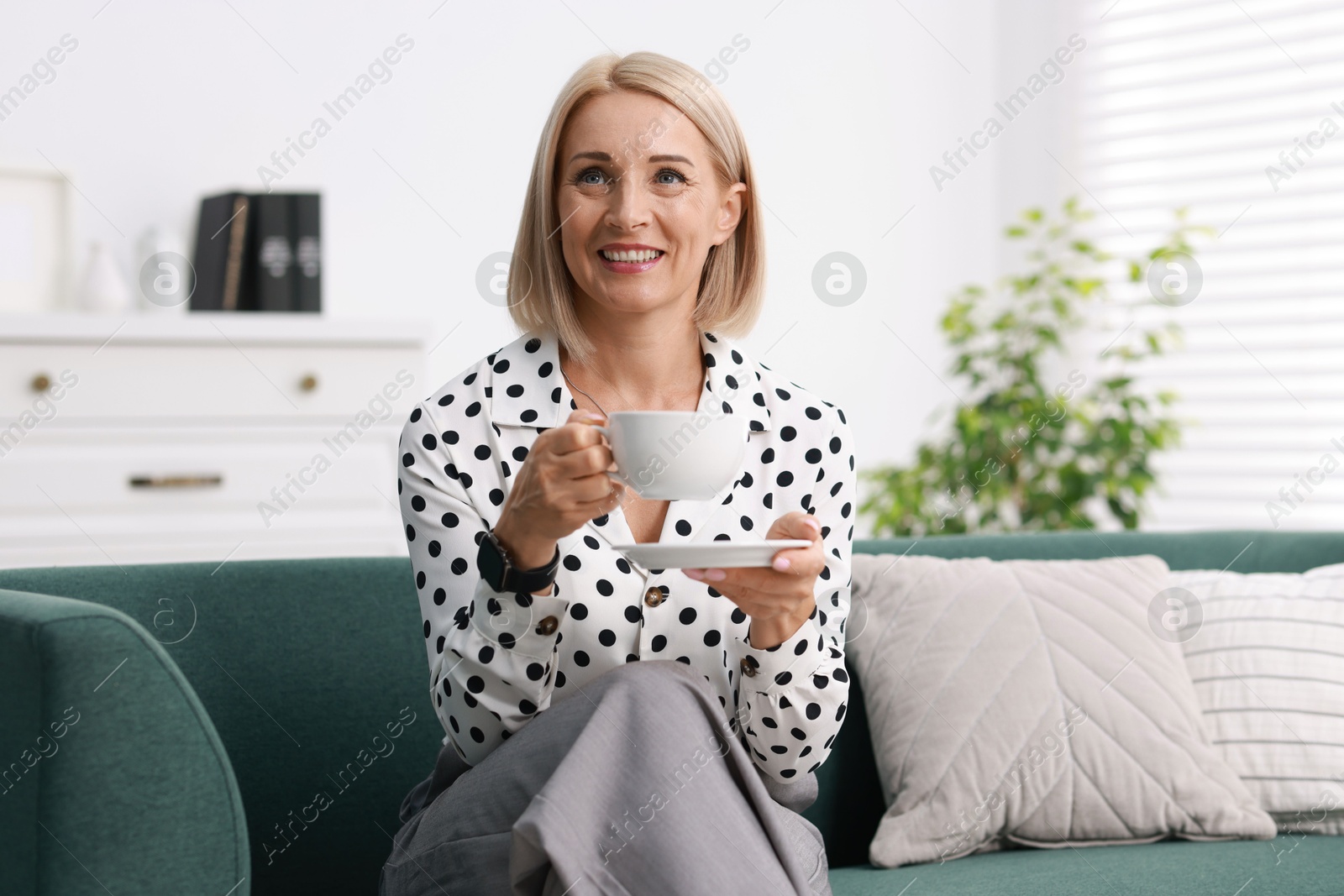 Photo of Smiling middle aged woman with cup of hot drink on sofa at home