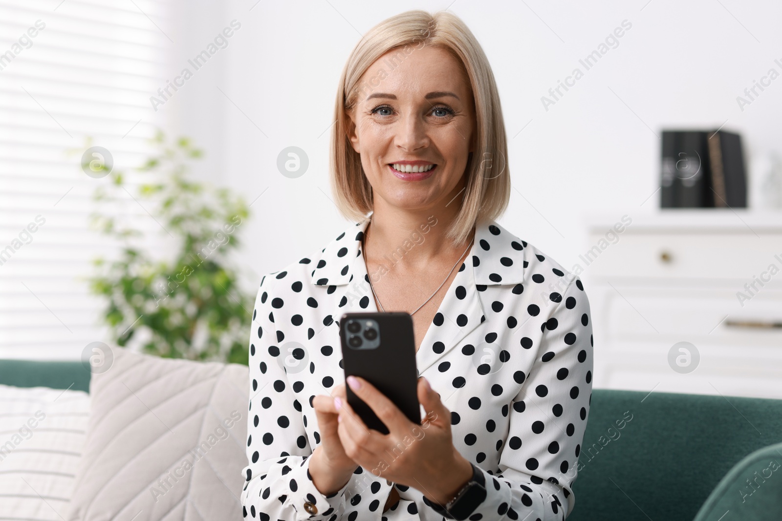 Photo of Portrait of smiling middle aged woman using smartphone at home