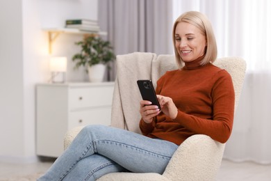 Portrait of smiling middle aged woman using smartphone on armchair at home