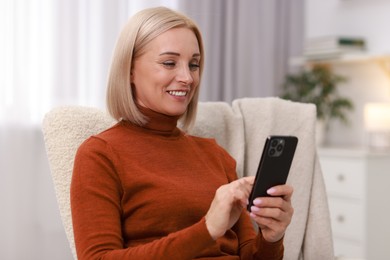 Photo of Portrait of smiling middle aged woman using smartphone at home