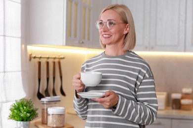 Smiling middle aged woman with cup of hot drink in kitchen