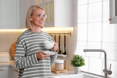 Photo of Smiling middle aged woman with cup of hot drink in kitchen