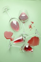 Photo of Glasses with spilled red wine on light green background, flat lay