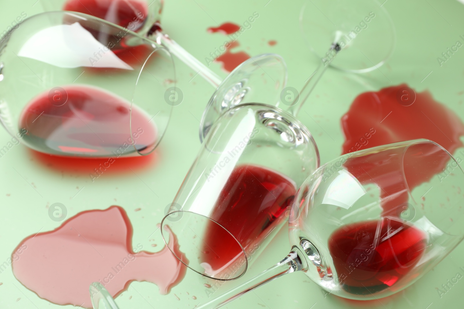 Photo of Glasses with spilled red wine on light green background, closeup