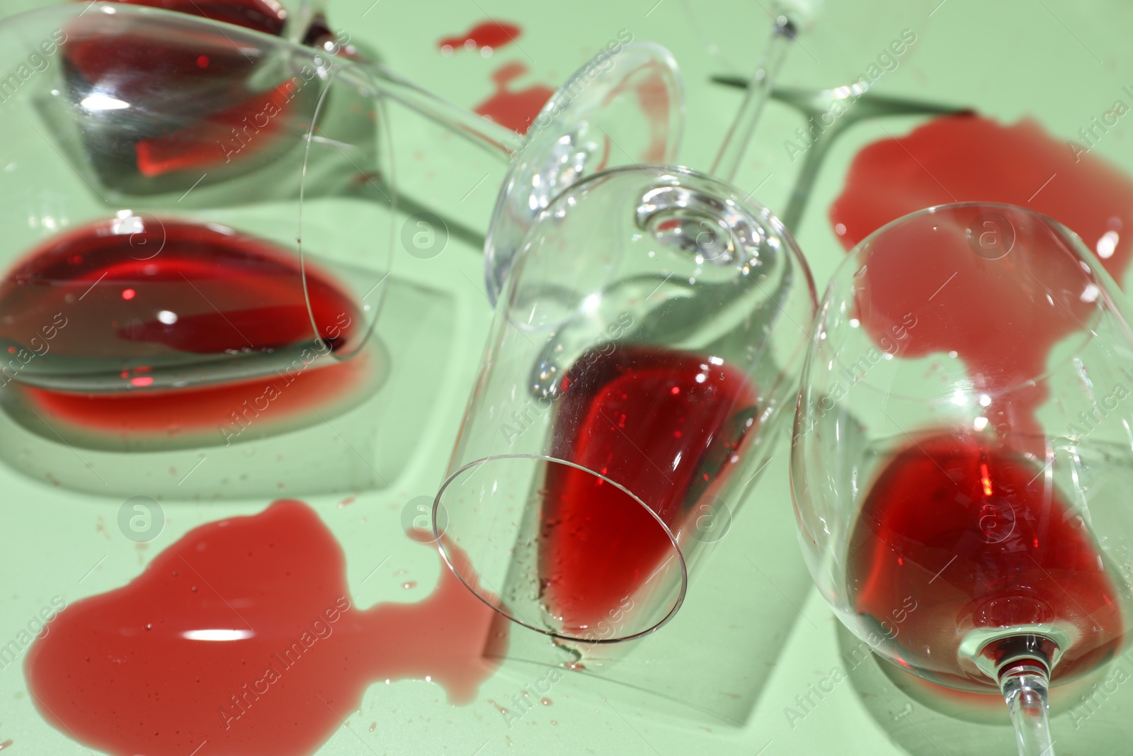 Photo of Glasses with spilled red wine on light green background, closeup