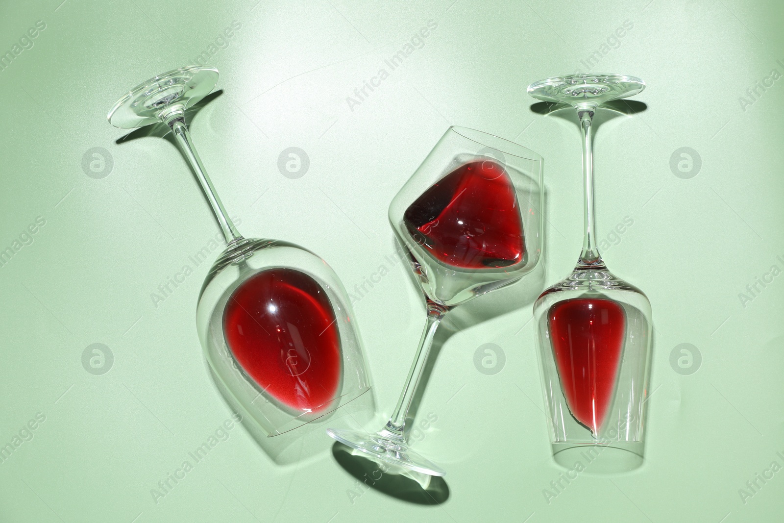 Photo of Glasses of red wine on light green background, flat lay