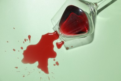 Photo of Glass with spilled red wine on light green background, top view