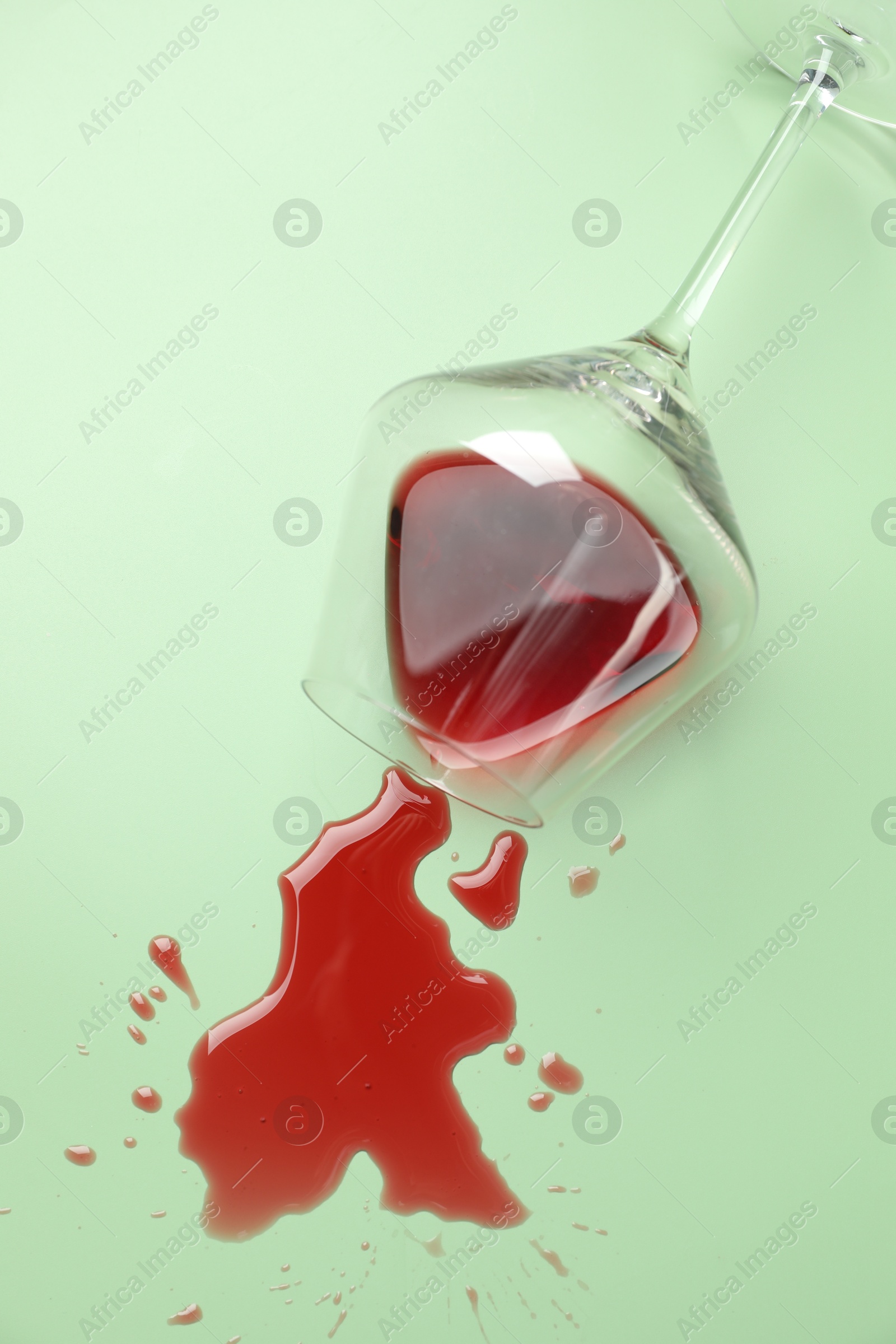 Photo of Glass with spilled red wine on light green background, top view