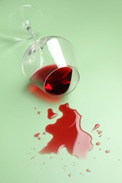 Photo of Glass with spilled red wine on light green background, closeup