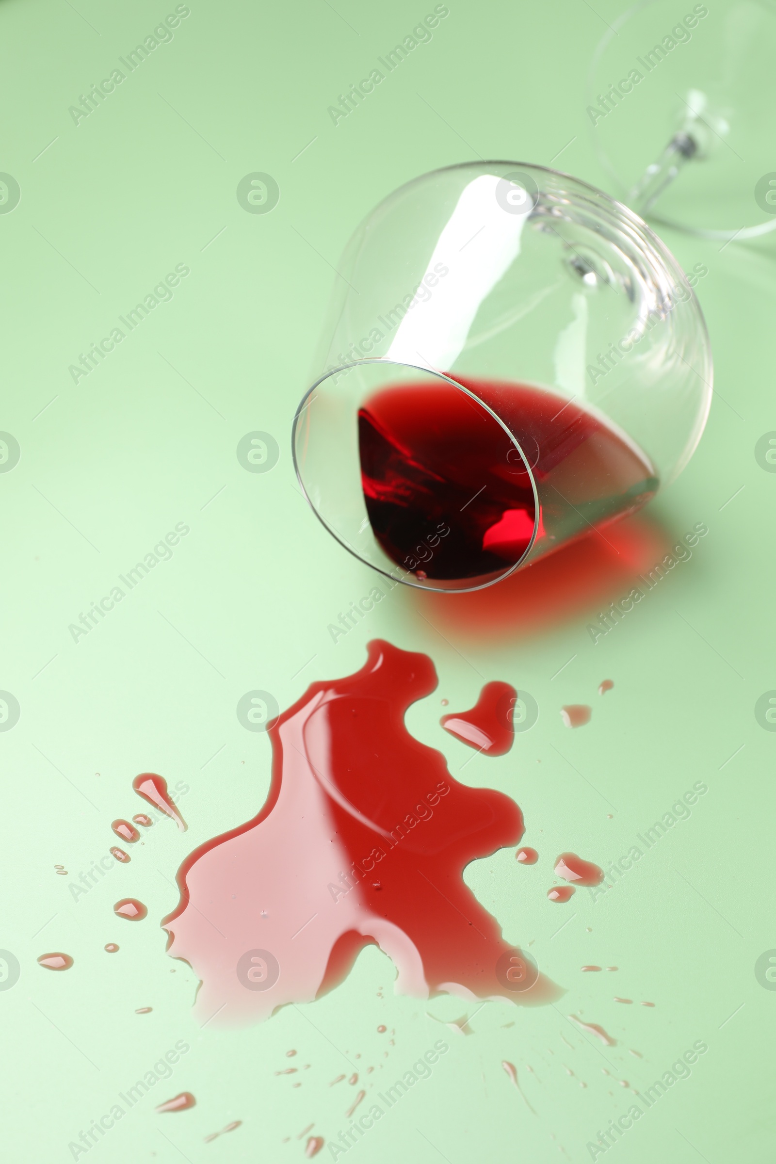 Photo of Glass with spilled red wine on light green background, closeup