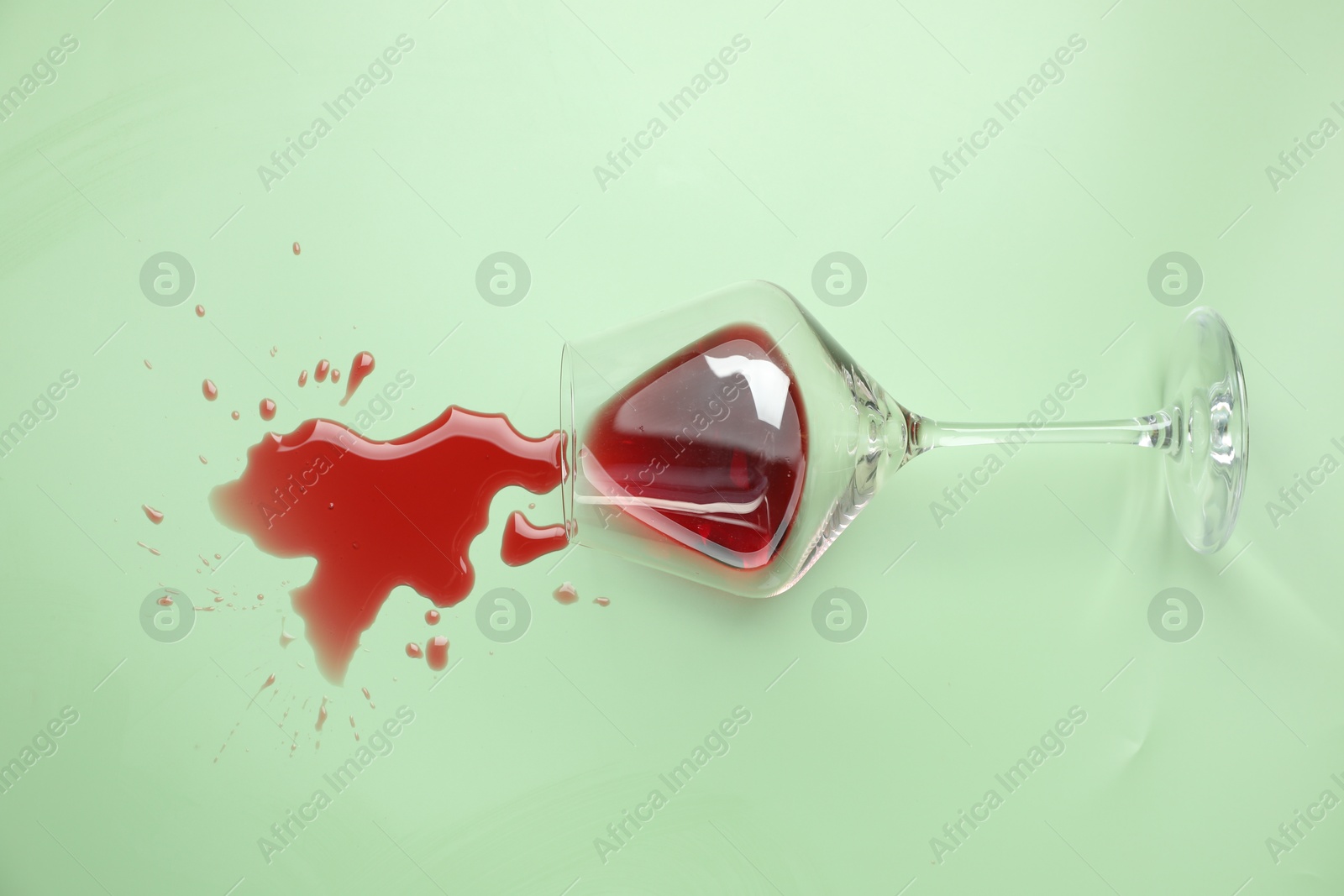 Photo of Glass with spilled red wine on light green background, top view