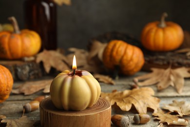 Photo of Autumn atmosphere. Burning pumpkin shaped candle and dry leaves on wooden table, closeup