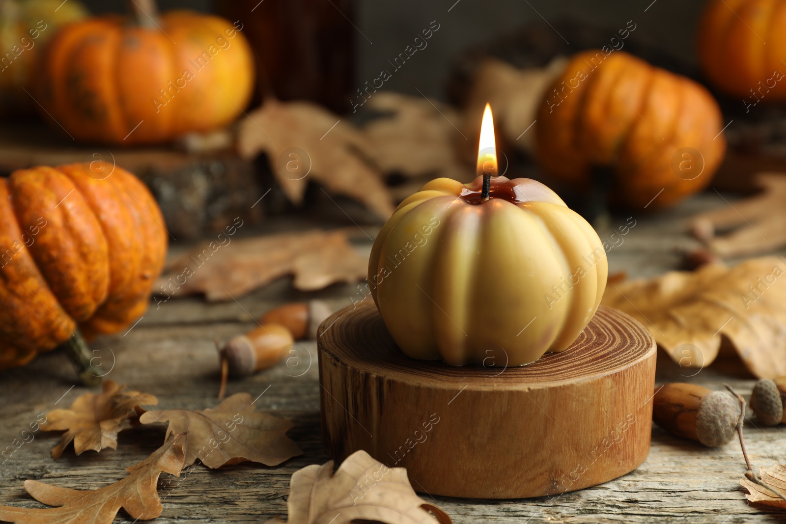 Photo of Autumn atmosphere. Burning pumpkin shaped candle and dry leaves on wooden table, closeup