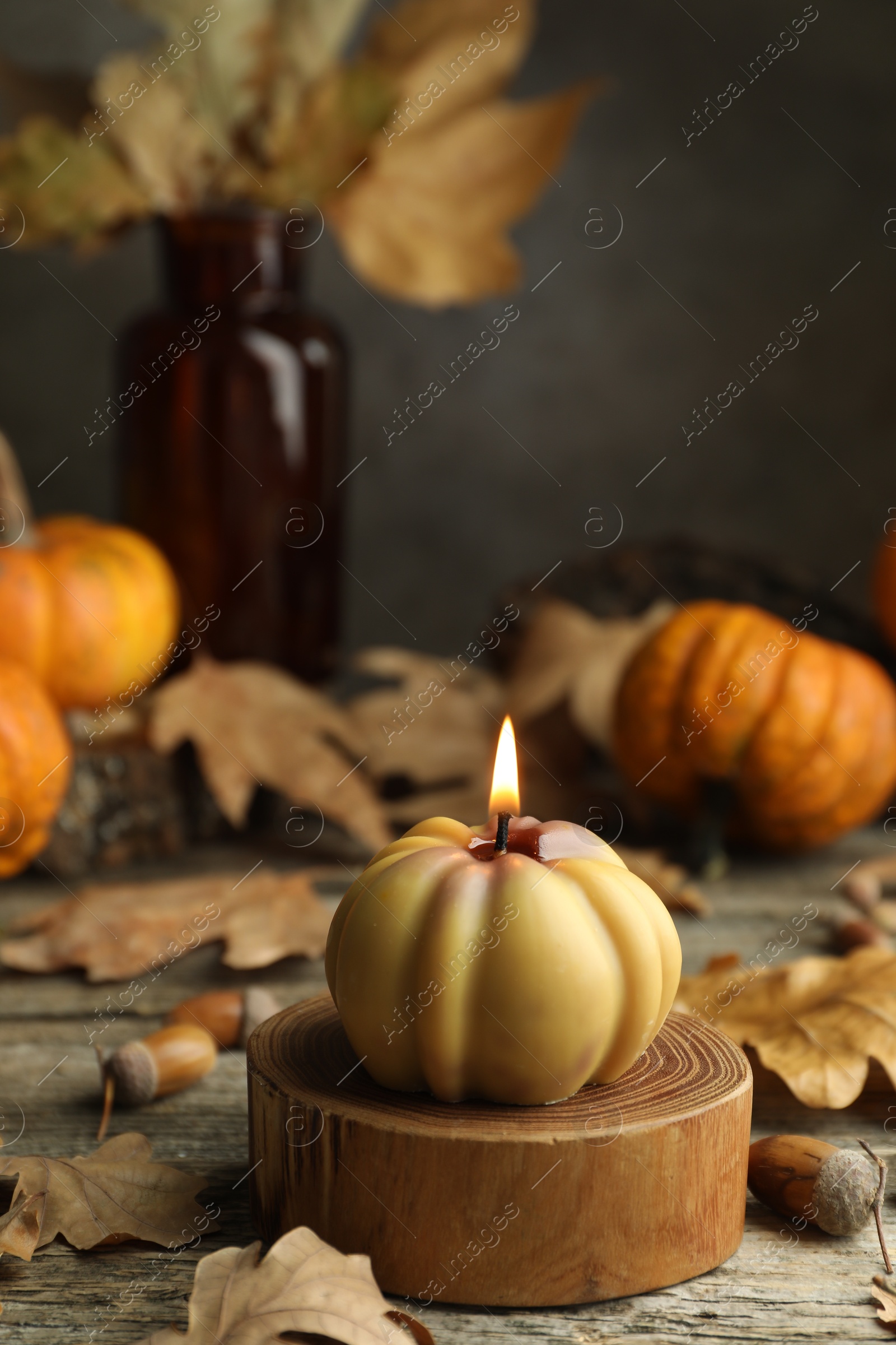 Photo of Autumn atmosphere. Burning pumpkin shaped candle and dry leaves on wooden table