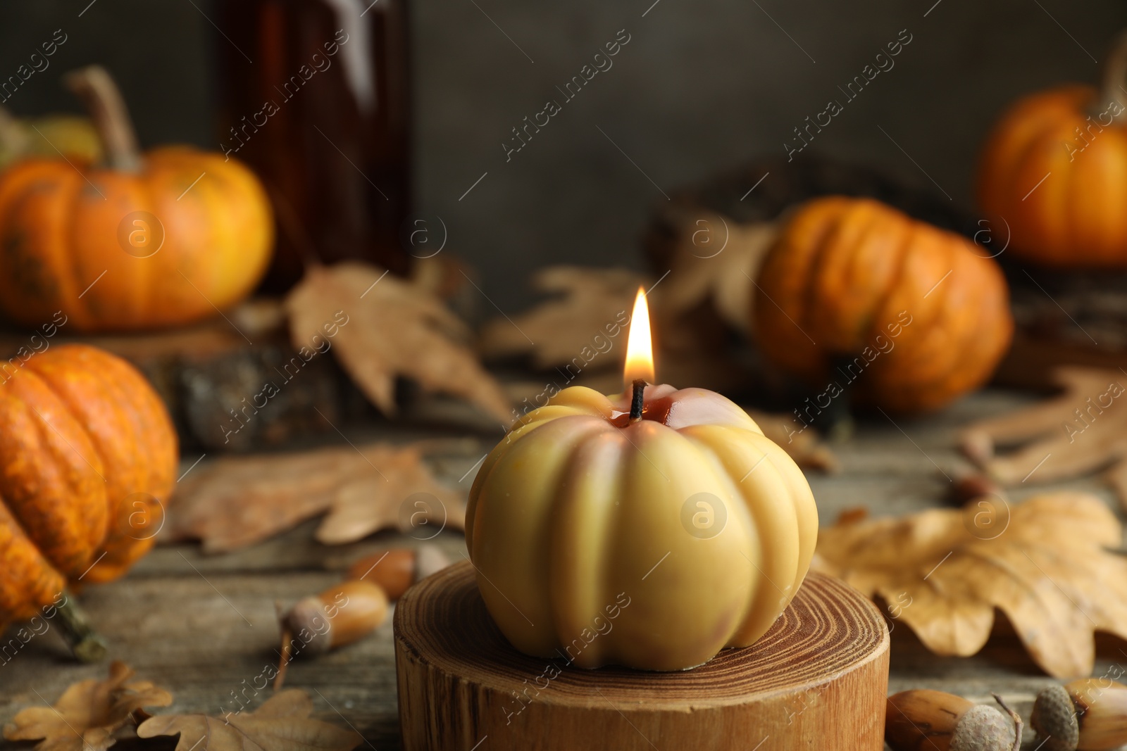 Photo of Autumn atmosphere. Burning pumpkin shaped candle and dry leaves on wooden table, closeup