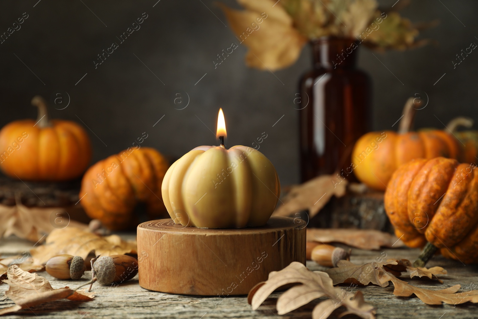 Photo of Autumn atmosphere. Burning pumpkin shaped candle and dry leaves on wooden table