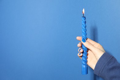 Photo of Woman holding burning candle on blue background, closeup. Space for text