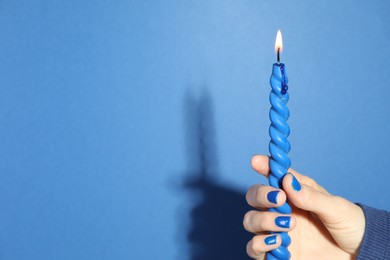 Photo of Woman holding burning candle on blue background, closeup. Space for text