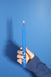 Photo of Woman holding burning candle on blue background, closeup