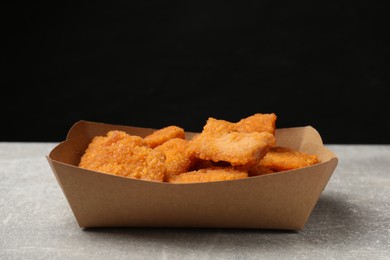 Delicious chicken nuggets in carton box on gray textured table against black background