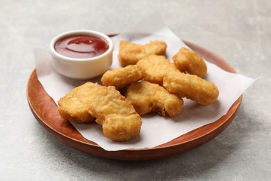 Photo of Delicious chicken nuggets and ketchup on gray textured table, closeup