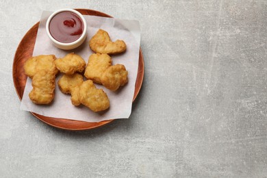 Photo of Delicious chicken nuggets and ketchup on gray textured table, top view. Space for text