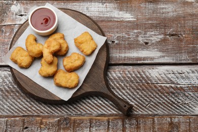 Delicious chicken nuggets and ketchup on wooden table, top view. Space for text