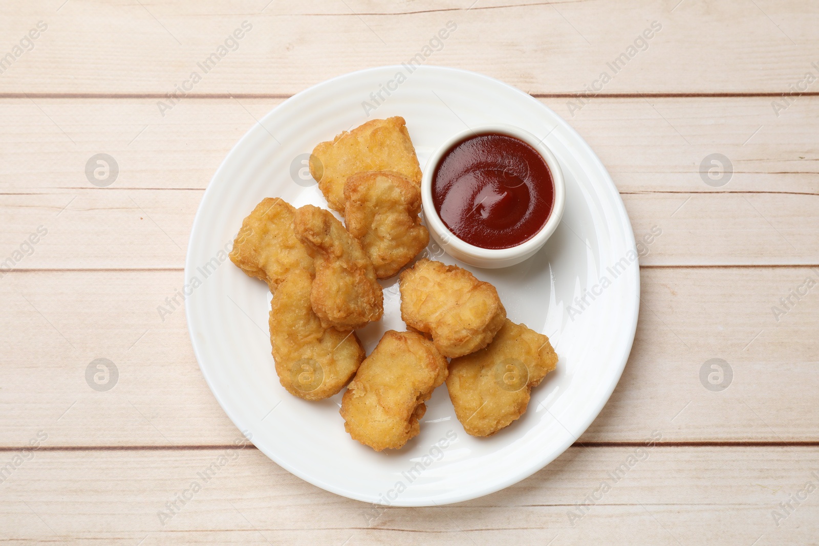 Photo of Delicious chicken nuggets and ketchup on wooden table, top view