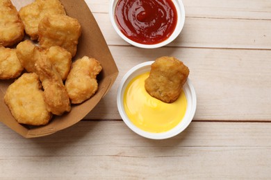 Photo of Delicious chicken nuggets in carton box and sauces on wooden table, flat lay