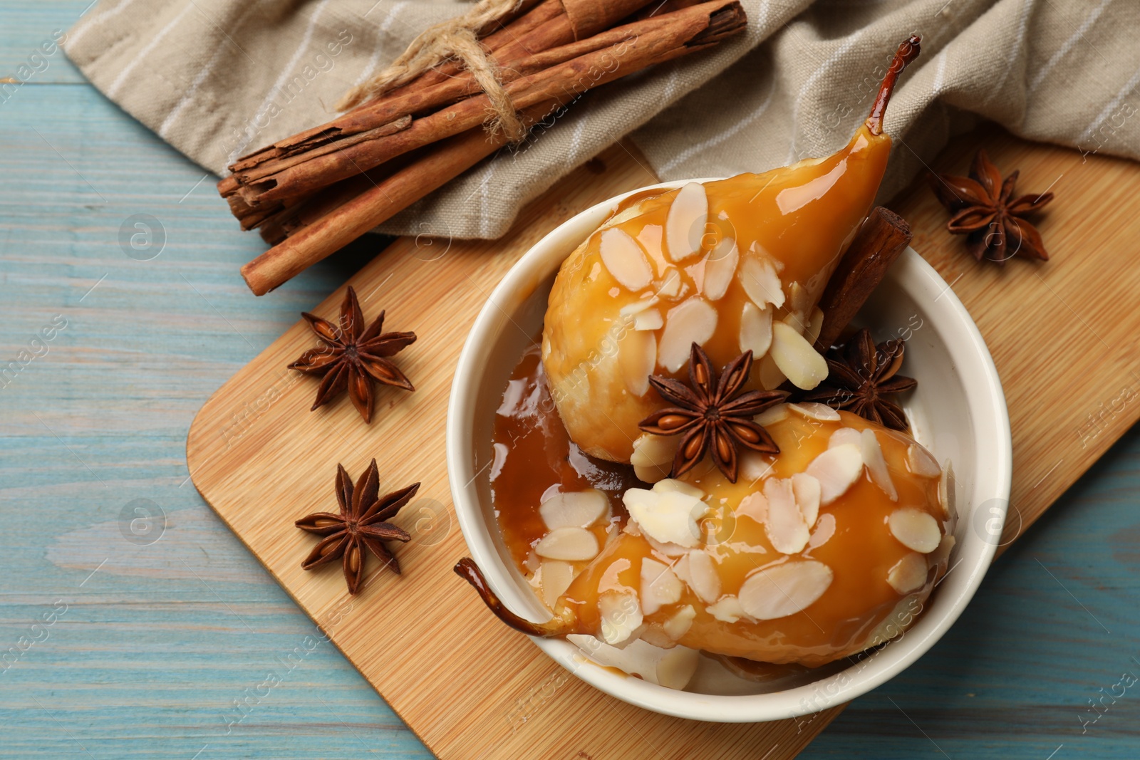 Photo of Delicious pears with caramel sauce, almond flakes and spices on blue wooden table, flat lay