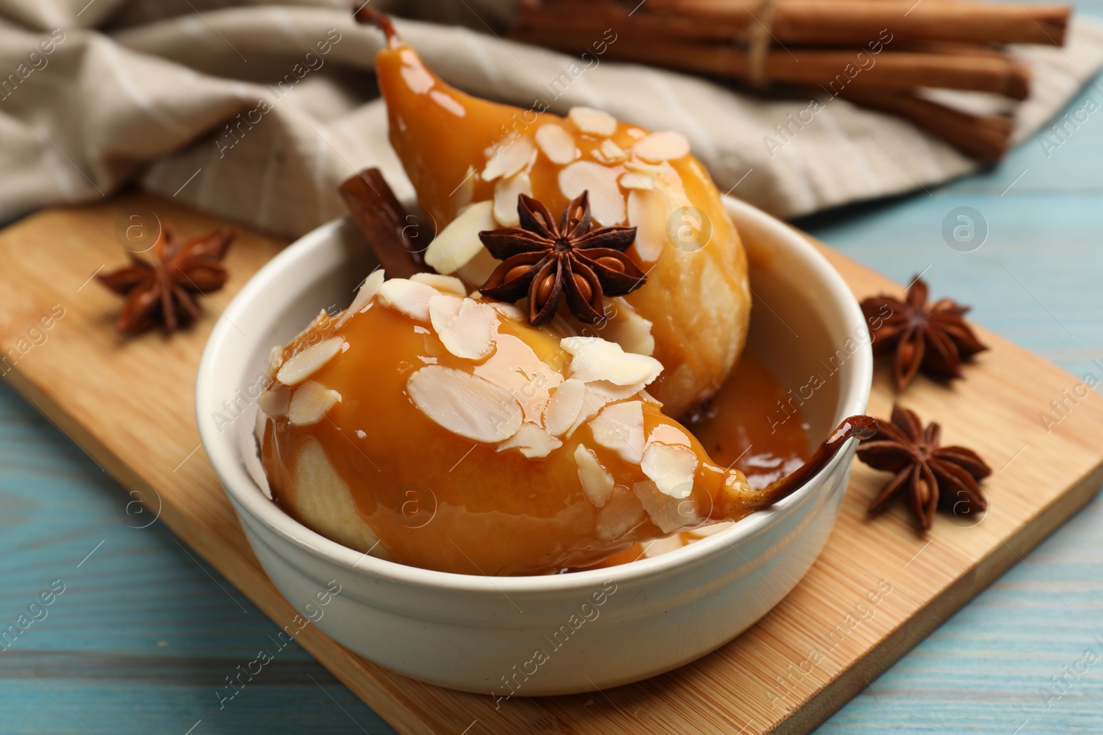 Photo of Delicious pears with caramel sauce, almond flakes and spices on blue wooden table, closeup