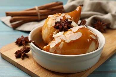 Photo of Delicious pears with caramel sauce, almond flakes and spices on blue wooden table, closeup