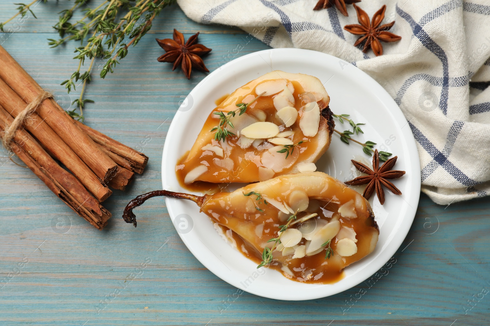 Photo of Delicious pears with caramel sauce, almond flakes and spices on blue wooden table, flat lay