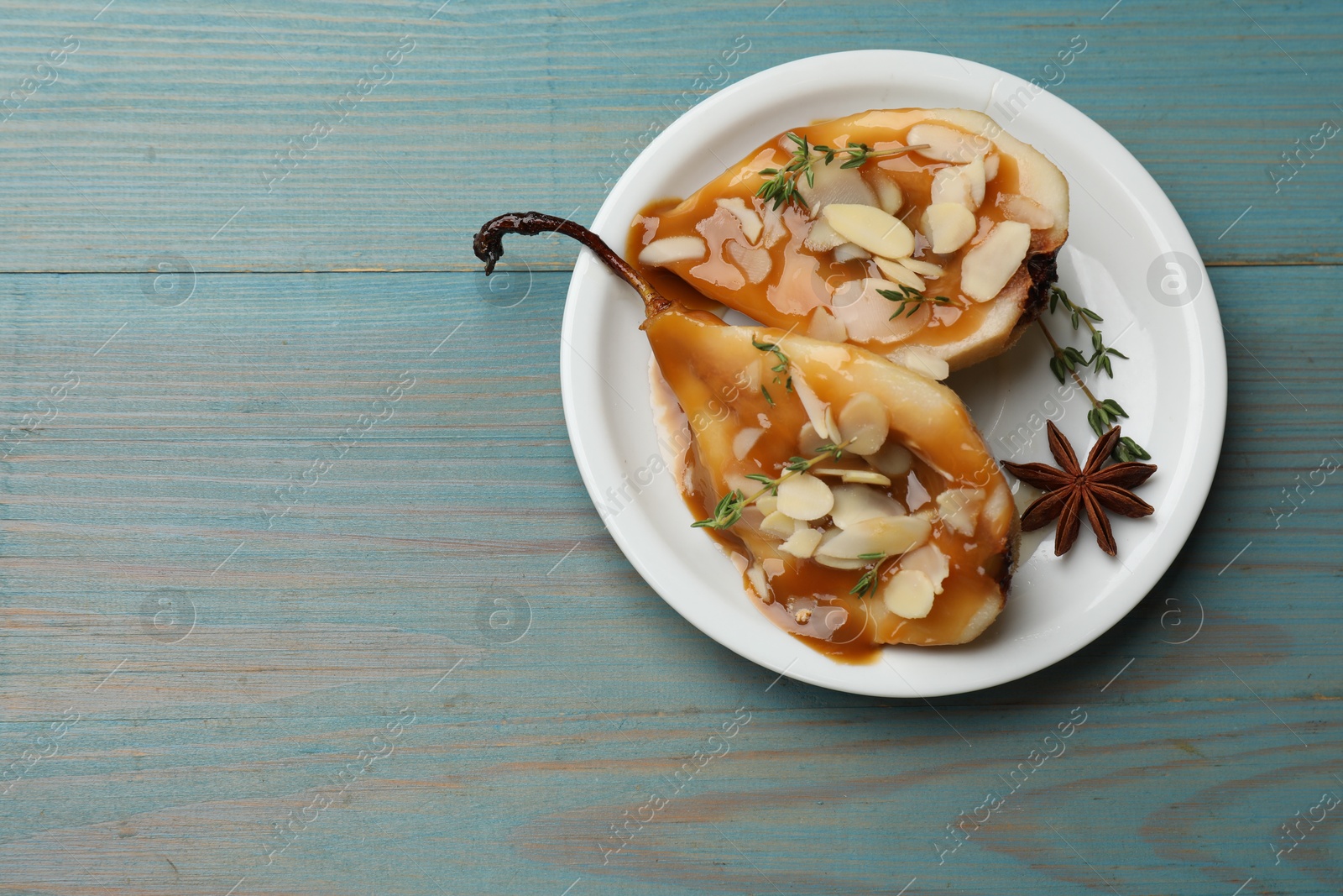 Photo of Delicious pears with caramel sauce, almond flakes and spices on blue wooden table, top view. Space for text