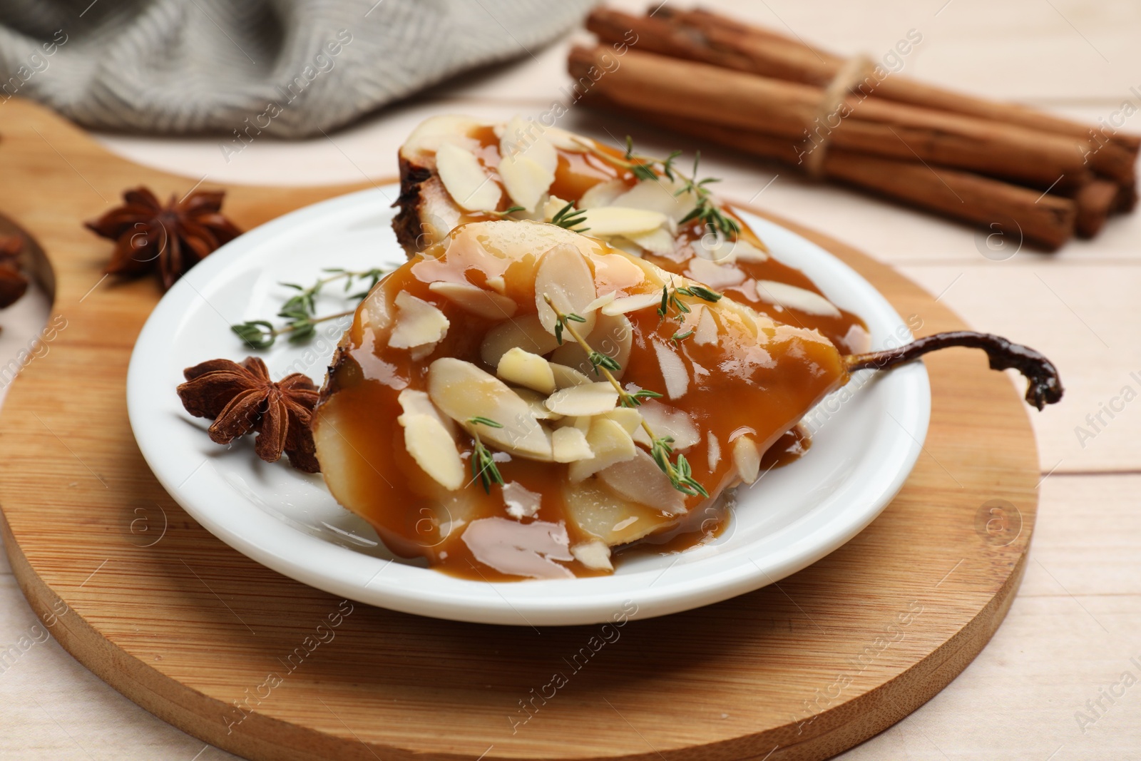 Photo of Delicious pears with caramel sauce, almond flakes and spices on white wooden table, closeup