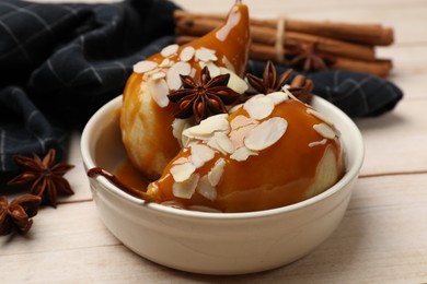 Photo of Delicious pears with caramel sauce, almond flakes and spices on white wooden table, closeup