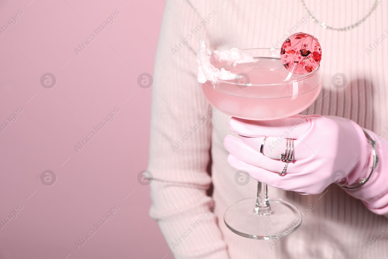 Photo of Woman holding glass of drink on pink background, closeup. Space for text