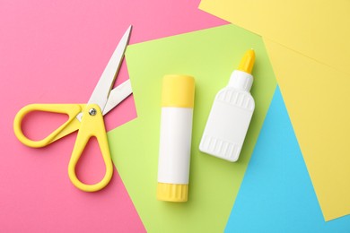 Glue, colorful paper and scissors on pink background, flat lay