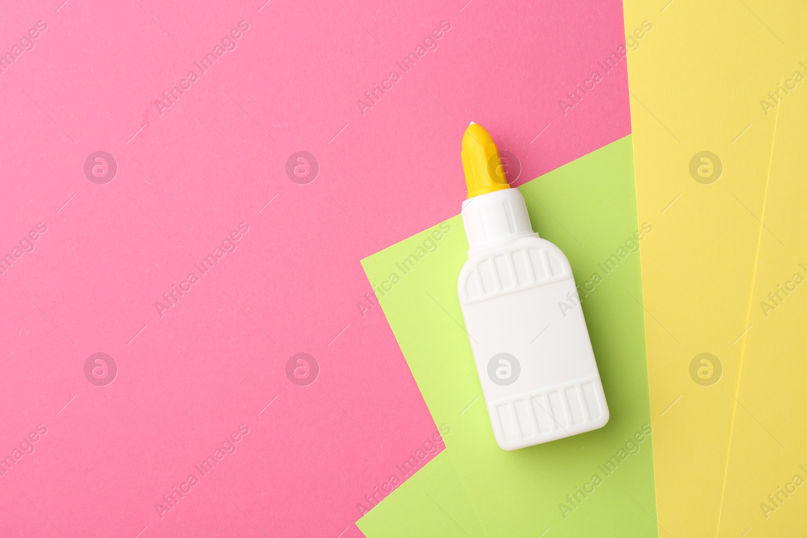 Photo of Bottle of glue and colorful paper on pink background, top view. Space for text