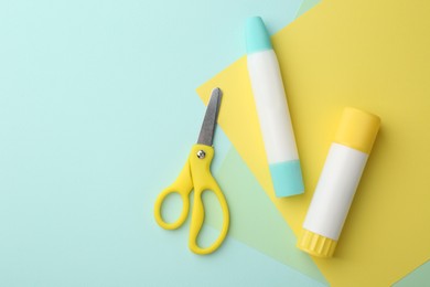 Photo of Glue, colorful paper and scissors on turquoise background, flat lay. Space for text