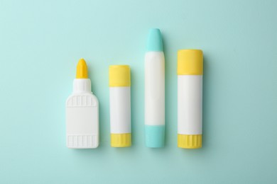 Photo of Different types of glue on turquoise background, flat lay