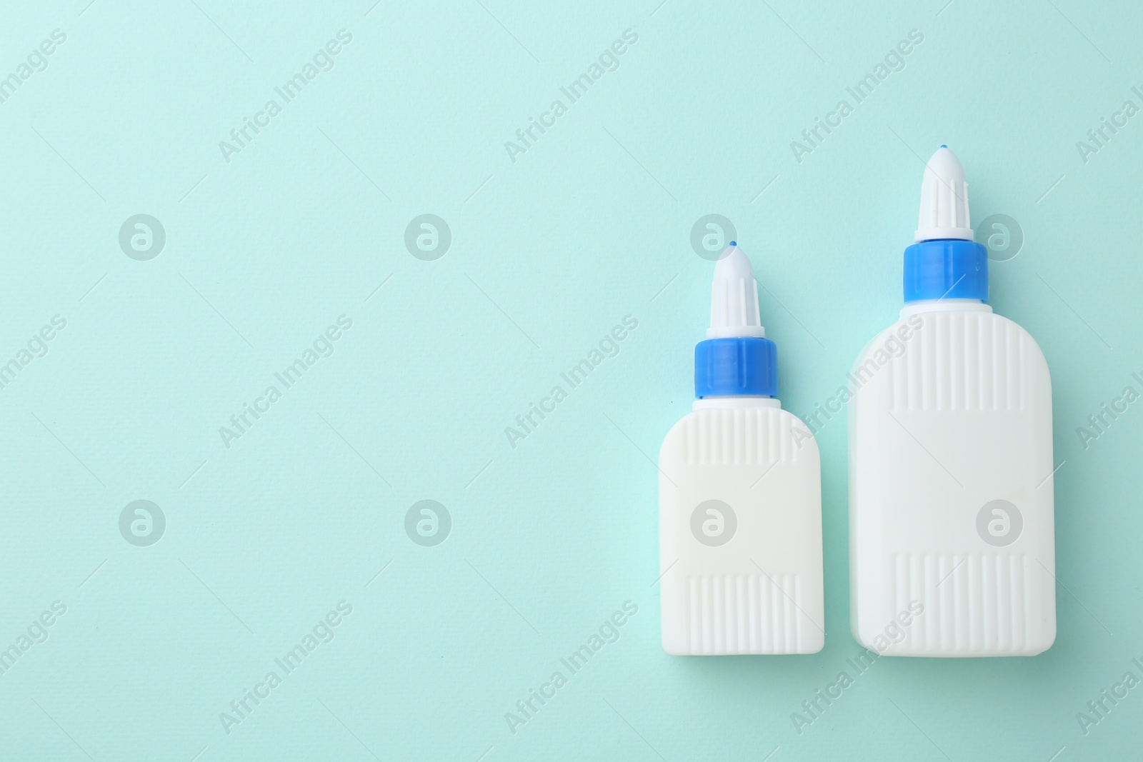 Photo of Bottles of glue on turquoise background, flat lay. Space for text