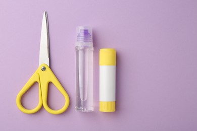 Glue and scissors on violet background, flat lay. Space for text