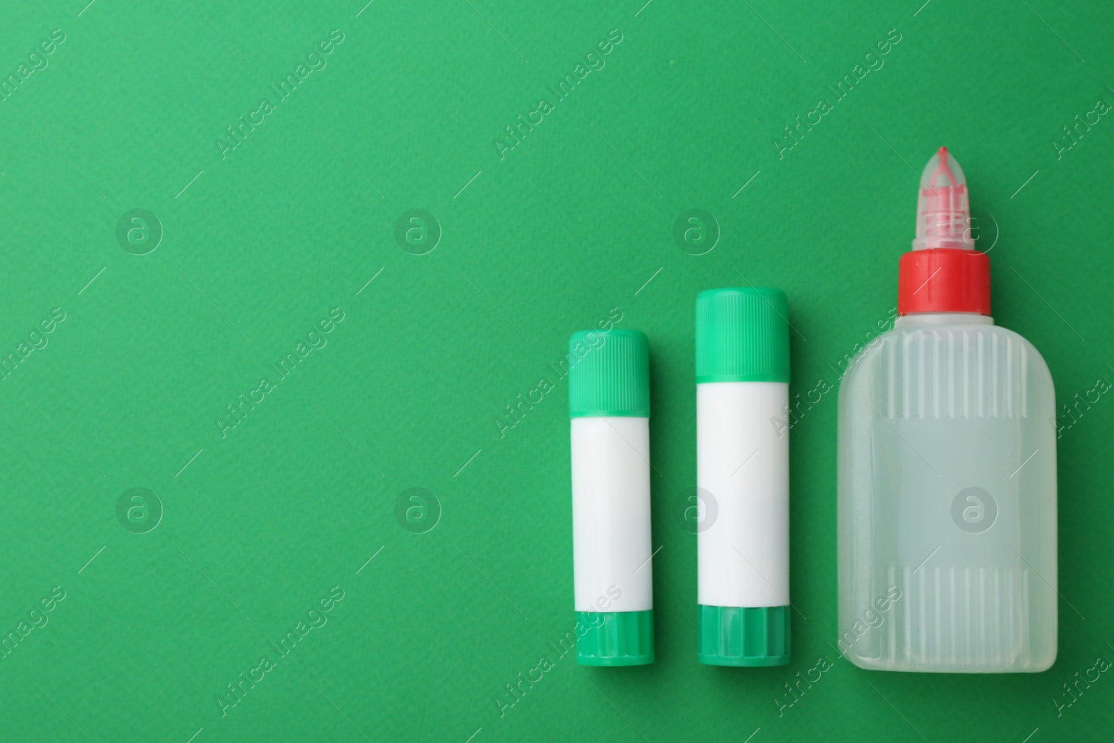 Photo of Different types of glue on green background, flat lay. Space for text