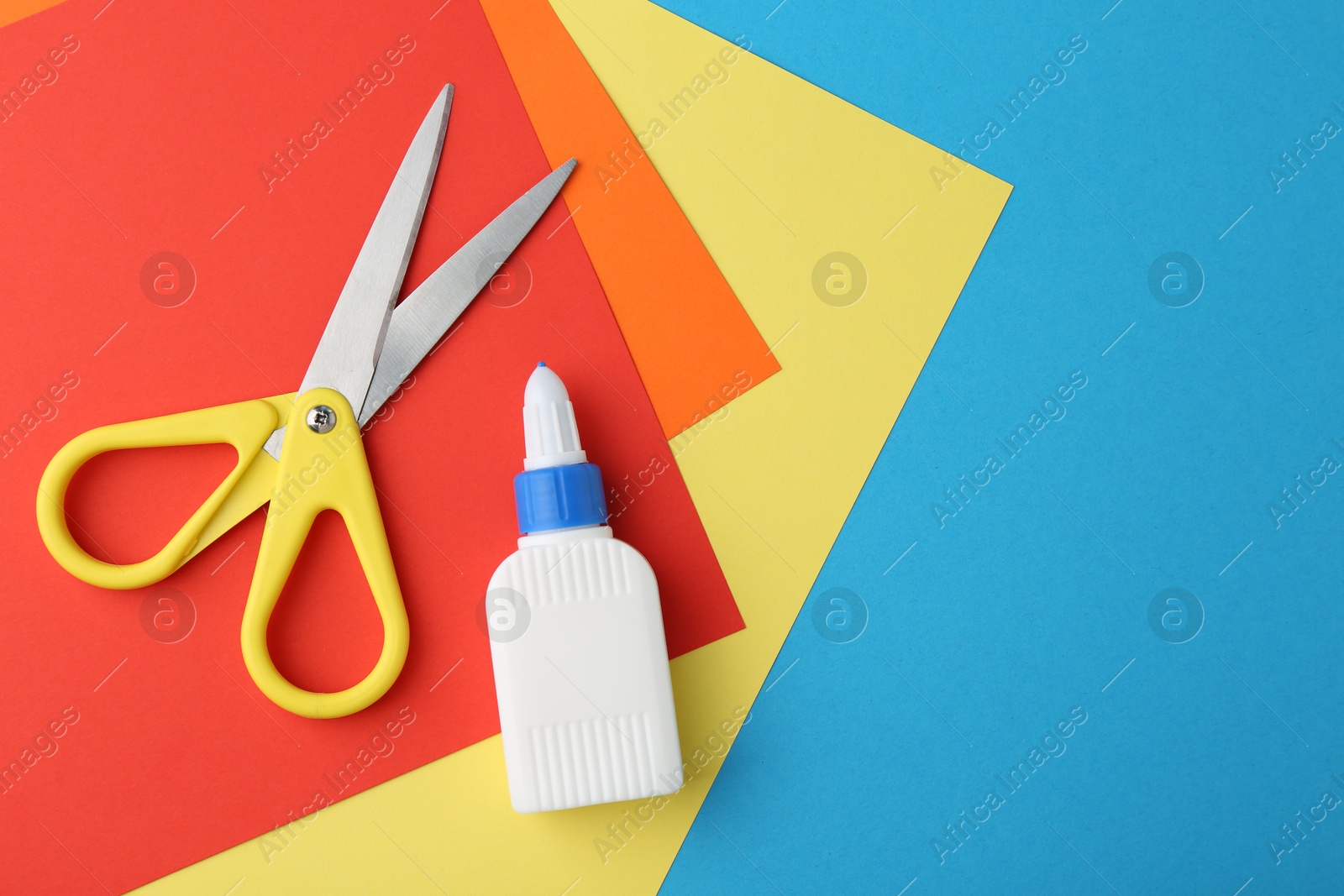 Photo of Glue, colorful paper and scissors on light blue background, flat lay. Space for text