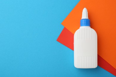 Photo of Bottle of glue and colorful paper on light blue background, top view. Space for text