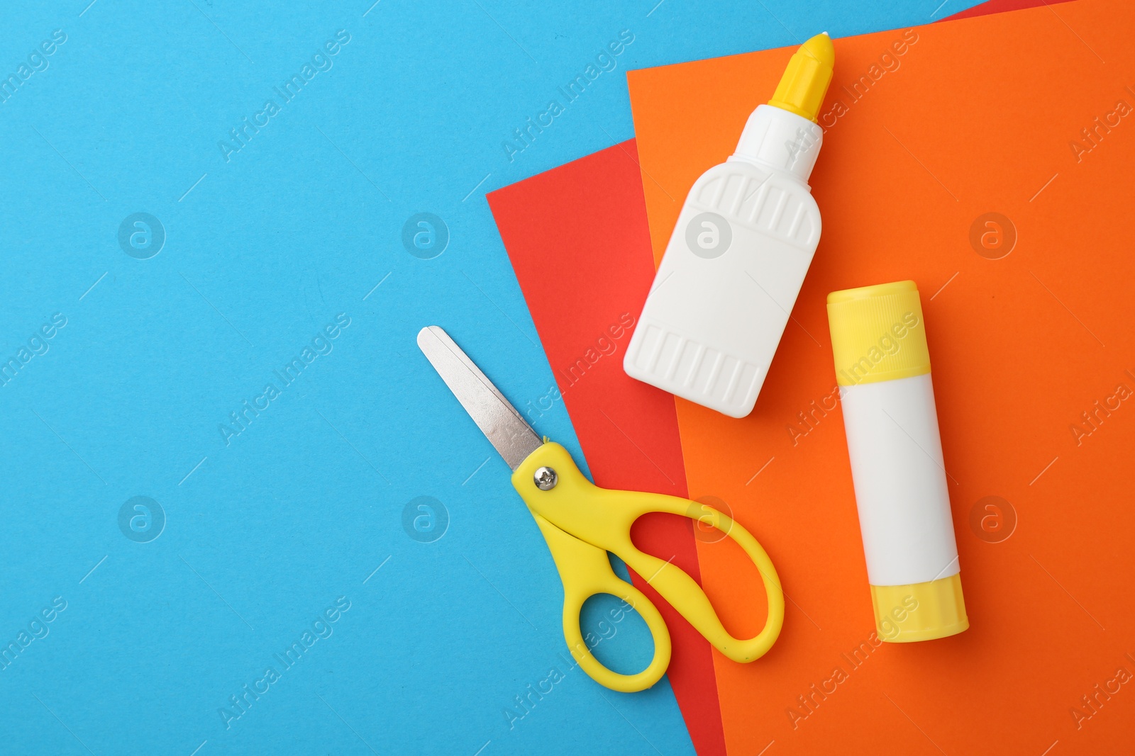 Photo of Glue, colorful paper and scissors on light blue background, flat lay. Space for text